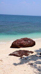 Rust-colored coastal rocks lie on white sand beside turquoise water © Utkarsh