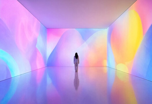 Woman standing in immersive digital art room with soft gradient pastel light projections.