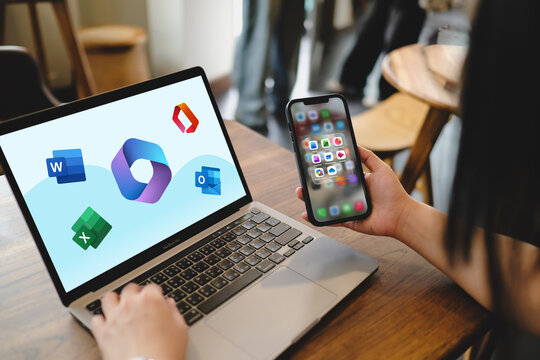 Bangkok, Thailand. August 16, 2026; Person holding smartphone and working on laptop both displaying Microsoft 365 office software application icons.