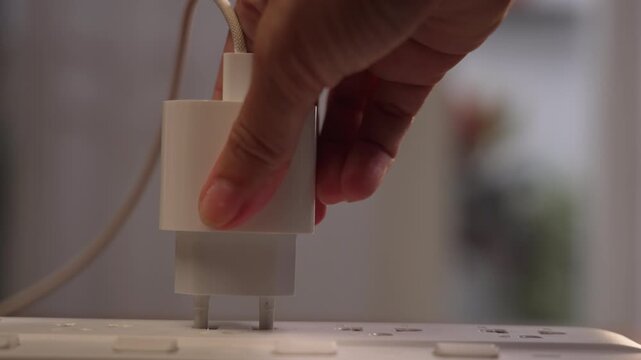 Centered close up of woman hand pushing adapter into power strip socket with difficulty, finally plugging in, success concept.⁠