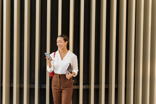Korean woman enjoying a sunny day checking her phone by modern buildings