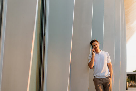 Young man enjoying a conversation while leaning against modern architecture