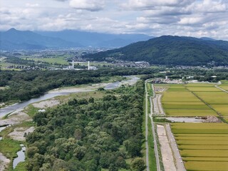 Lush rice fields stretch beside a winding river. Distant mountains frame the tranquil countryside. Clouds drift lazily over verdant hills and villages © Masakazu Tokashiki