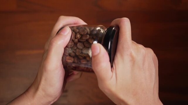 Centered top view of woman hands holding coffee bean glass jar on wooden desk, straining wrist muscles to twist stuck tight lid, deadlock concept.⁠