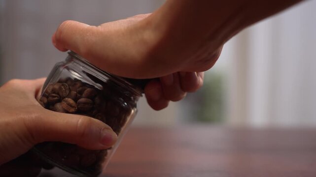 Extreme close up macro on left side with copy space of woman hands holding coffee glass jar, straining to twist tight cap until grip slips, frustration concept.⁠