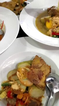 Vertical close up of pouring coconut milk broth over traditional Indonesian chicken curry and rice cakes Lontong Sayur