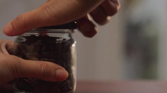 Extreme close up macro on left side of woman hand supporting coffee glass jar on wooden desk, showing intense finger pressure while twisting stuck lid, deadlock concept.
