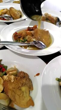 Vertical close up of pouring coconut milk broth over traditional Indonesian chicken curry and rice cakes Lontong Sayur