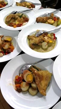 Vertical pan over dozens of plated traditional Indonesian chicken curry dishes ready for catering service in commercial kitchen