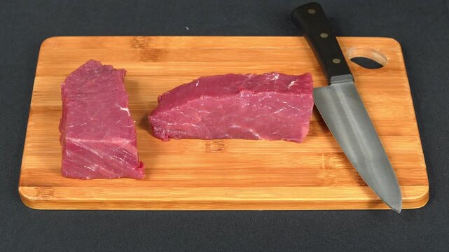 Slices of fresh raw beef meat and chef knife placed on wooden cutting board, top view.