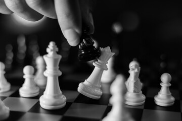 Black and white chess game showing hand moving black knight among white pieces on checkered board, creating strategic tension and competitive focus in close view © CoreRock