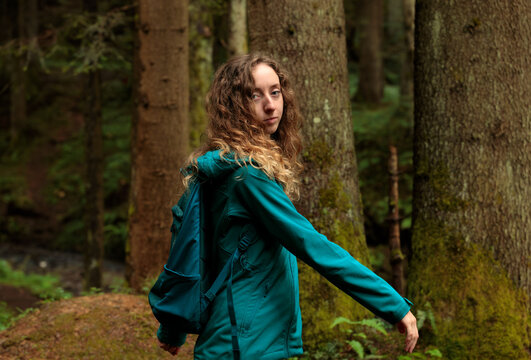 young woman with curly hair enjoys cheeling peaceful moment while hiking in a dense forest feeling the freedom of nature