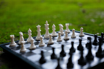Chess board with white and black pieces arranged for outdoor strategy game, surrounded by soft green grass and natural light, creating focused competitive atmosphere © CoreRock