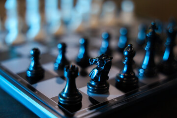Chess piece on digital chessboard with blue lighting and shallow depth of field, creating dramatic strategy game scene with reflective black pieces and blurred background © CoreRock