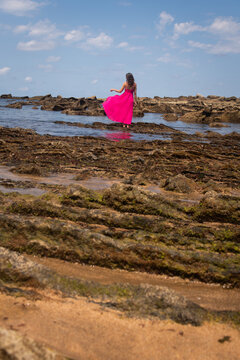 woman in pink dress on flysch rock plates on itzurun beach near zumaia in basque country, spain