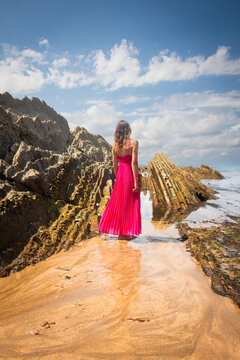art model in pink dress between flysch cliffs of itzurun beach near zumaia in basque country, spain