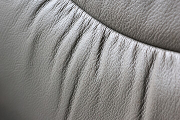 Gray leather upholstery texture with gathered seam detail, soft material surface and curved cushion closeup showing fine grain and tactile structure © CoreRock