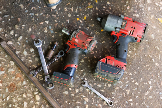 Power tool cordless drill impact driver hand tool wrench battery workshop equipment arranged worn concrete floor, showing repair work, maintenance, mechanical service, and practical trade