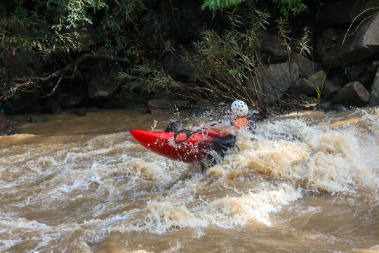 Red kayak white helmet whitewater kayaking rapid river river spray outdoor adventure red kayak navigating turbulent rapid water with helmeted paddler surrounded by forest, rock and foamy current