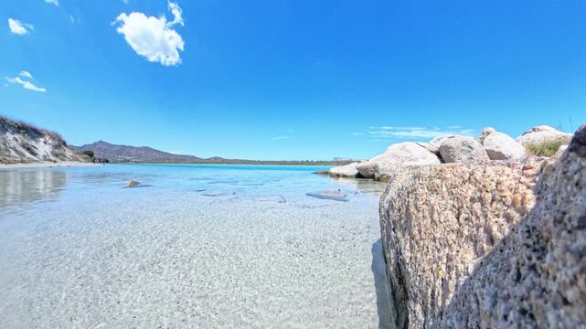 Serene seascape at La Cinta beach San Teodoro Sardinia with rock in foreground and mountains under single cloud