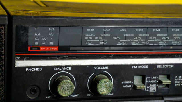 Detailed frontal shot of an antique portable stereo displaying a scratched tuning frequency panel alongside heavily oxidized control knobs and mode selector switches. Set against a