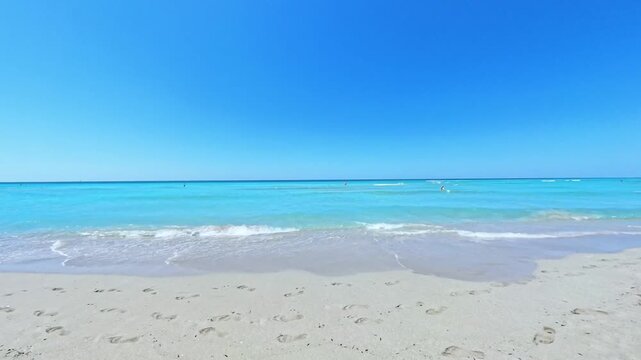 Turquoise Mediterranean sea gently lapping shore at Riva di Ugento beach in Puglia southern Italy with distant beachgoers