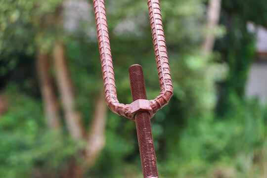 Rusty steel rebar connector with threaded rod outdoors against blurred green woodland background
