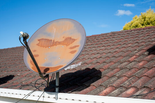 Rusted satellite dish atop a tiled roof