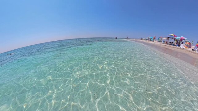 Walking POV Mari Ermi beach Sardinia wider view with colorful beach umbrellas in distance