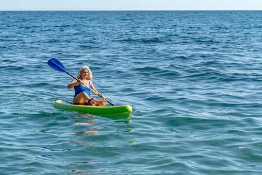 Mature woman paddling lime green kayak across blue ocean water during summer day outdoor activity