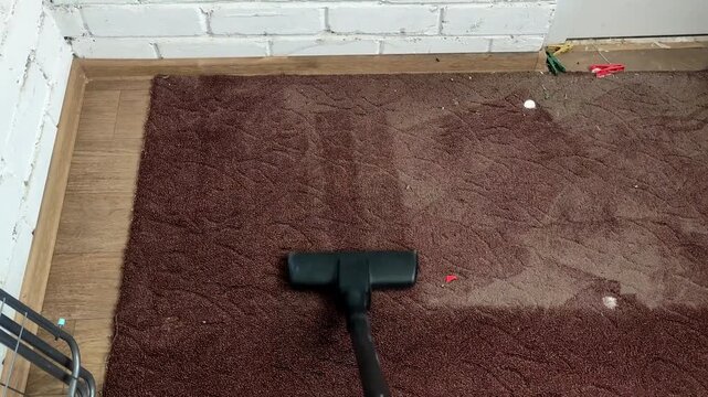 Person vacuuming old and dirty brown rug with a vacuum cleaner, first person view