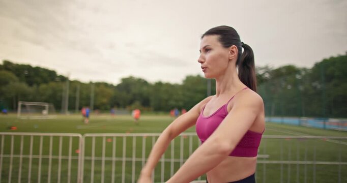 Young athletic woman in sportswear warming up and doing exercises on the stadium running track in the evening at sunset