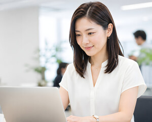 Obraz premium Smiling Japanese businesswoman working on laptop in bright modern office with copy space