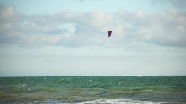 Kiteboarding, Ocean, Beach: A red kite flies high above a blue and green ocean on a cloudy day.