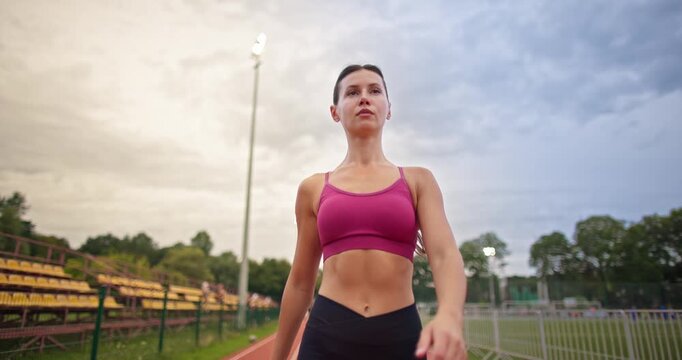 Young athletic woman in sportswear warming up and doing exercises on the stadium running track in the evening at sunset
