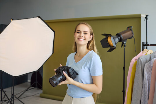 Photographer woman with camera in studio photoshoot. Modern lighting and equipment frame a fashion portrait set with backdrop, softbox and strobe. Concept is creative professional studio work.