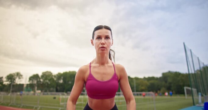 Young athletic woman in sportswear warming up and doing exercises on the stadium running track in the evening at sunset