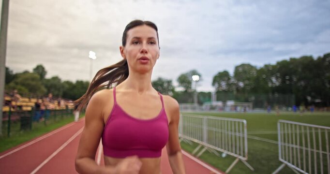 Young athletic woman in sportswear warming up and doing exercises on the stadium running track in the evening at sunset