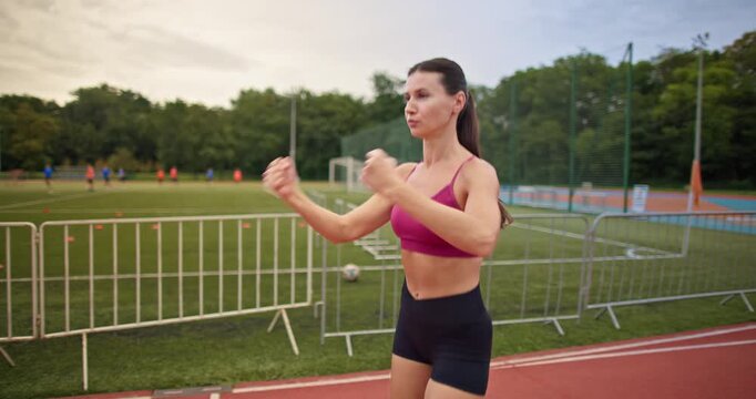 Young athletic woman in sportswear warming up and doing exercises on the stadium running track in the evening at sunset