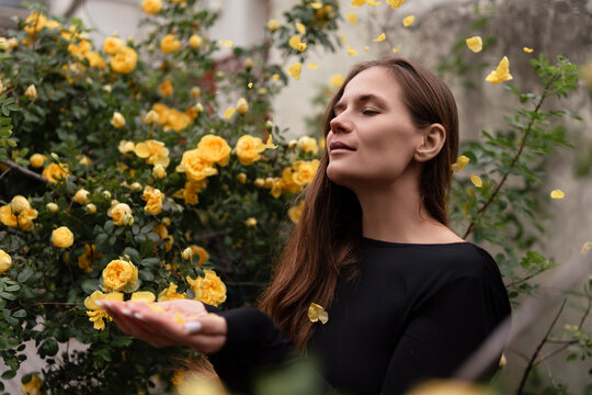 Tranquil woman catching yellow rose petals in a lush garden during a peaceful self care moment