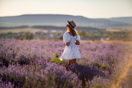 Woman lavender field walking summer dress straw hat enjoying rural sunset landscape