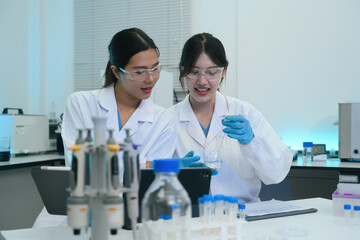 Fototapeta premium Two Asian Female Scientists Collaborating in Modern Laboratory, Examining Chemical Sample in Flask