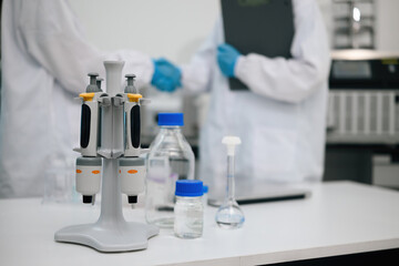 Fototapeta premium Micropipette Stand with Laboratory Glassware on White Bench and Scientist shanking hands in Background