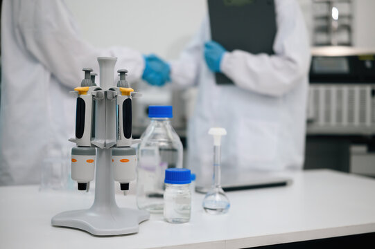 Micropipette Stand with Laboratory Glassware on White Bench and Scientist shanking hands in Background