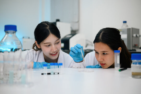 Two Asian Female Scientists Conducting Laboratory Experiment with Pipette and Test Tubes in Modern Lab