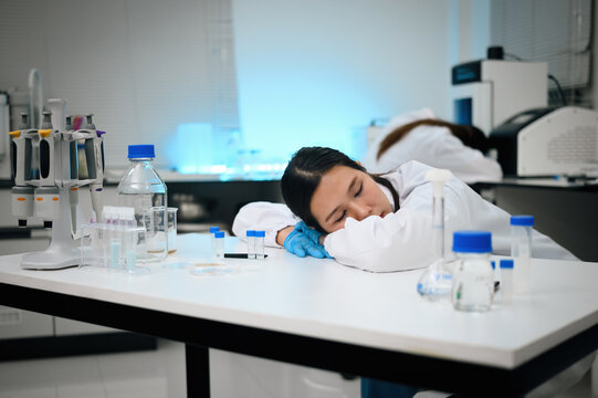 Exhausted Female Scientist Sleeping on Laboratory Bench Surrounded by Research Equipment