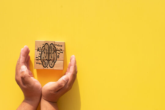 Hands protecting wooden blocks with a digital AI brain and circuit graphic overlay on a yellow background. Concept of artificial intelligence, machine learning, ethical AI, and technology innovation.