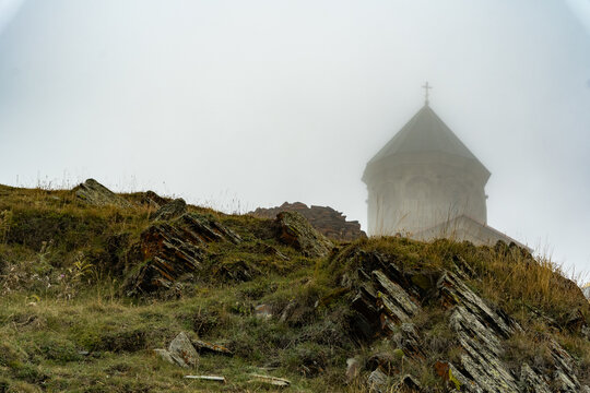 Gergeti Trinity Church tower in thick fog behind rocky mountain slope