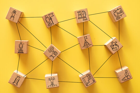 Wooden blocks with business strategy and leadership icons connected by lines on a yellow background. Concept of networking, action plan, and connecting the dots for success.