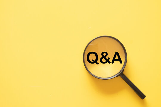 Top view of a magnifying glass focusing on the text Q&A on a yellow background with copy space. Concept of questions and answers, frequently asked questions, customer support, and problem solving.